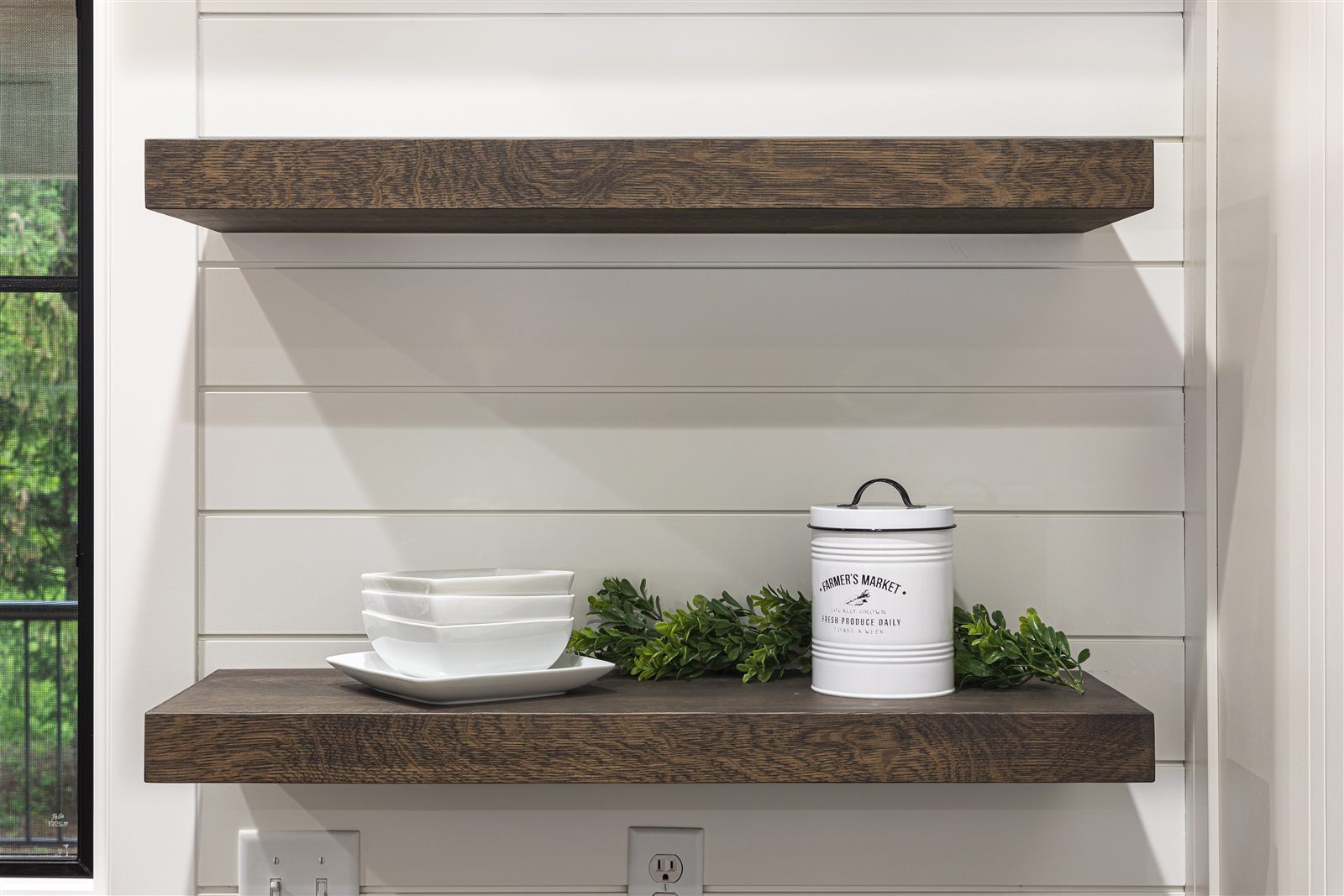 Two dark walnut floating shelves against white shiplap, styled with bowls, a canister, and greenery