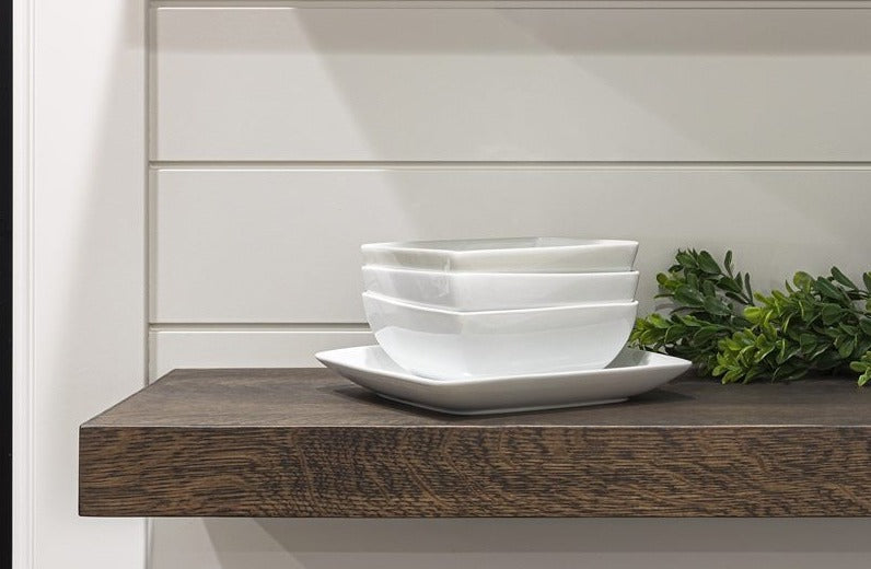 Floating shelf with a stack of white bowls, a plate, and greenery against a plain wall