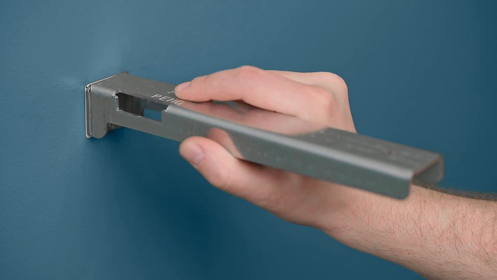 Raw steel floating shelf bracket held against a wall before installation